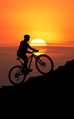 Obraz premium Silhouette of a cyclist riding uphill during a stunning sunset. The silhouette is a mountain bike rider on the top of the hill with a beautiful, vibrant sun as the backdrop