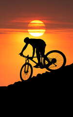 Obraz premium A cyclist silhouetted against a setting sun, mountain biking on the mountain