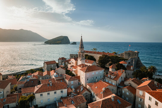 Aerial view of terracotta rooftops cascading towards the Adriatic Sea, framed by the medieval citadel and the distant Sveti Nikola Island, Budva, Budva Municipality, Montenegro.