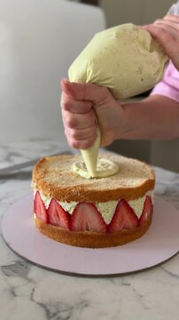 Top view of hands in pink chef shirt and apron piping pistachio cream on luxury fraisier cake. Premium dessert preparation, professional pastry styling