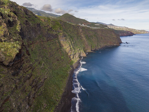 Aerial view of stark cliffs plunging into the dark blue sea, framing the black sands of Playa de Nogales below, La Palma, Canary Islands, Spain.