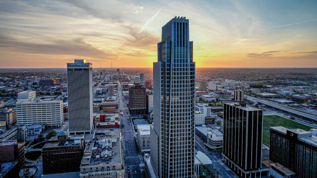 Aerial view of warm sunset hues paint the sky behind the First National Bank Tower and the Woodmen Tower, casting long shadows on the streets below, Omaha, Nebraska, United States.