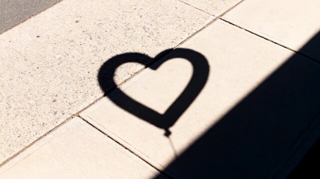 Drifting heart balloon shadow moving across pavement shifting string shadow creeping slanted shade