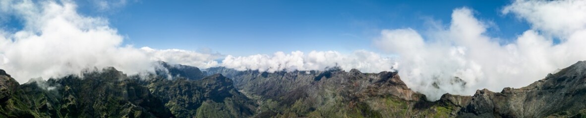 Obraz premium Drone super panorama of central Madeira highlands at Pico Ruivo Portugal, a sweeping ridge line with rocky summits rises through misty clouds in bright daylight