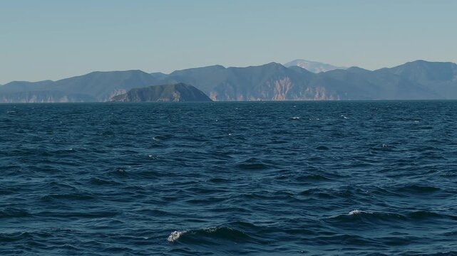 Panorama of sea bay with white yacht drifting on blue waves and view of coast with mountain ranges covered with greenery and volcanoes with snow-capped peaks. Concept of silence and pacification