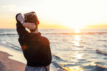 Back view young adult woman dreamy looking sunset horizon on sandy beach shore warm evening sunset light. Scenic wellbeing concept mindfulness balance hope emotional recovery mental health sea © Kyryl Gorlov