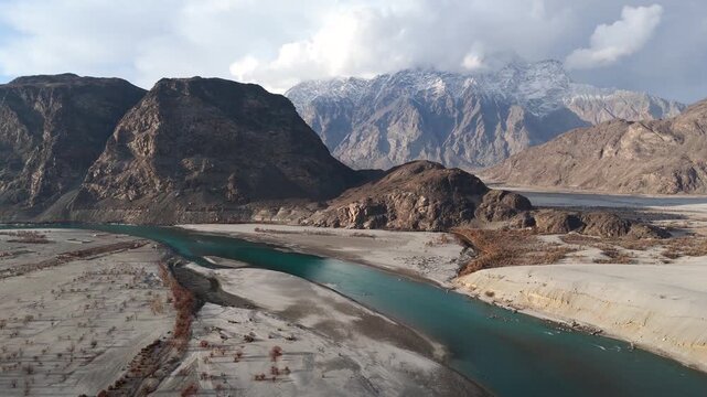 Aerial view of the Indus River flowing through a valley, contrasting with the barren landscape and towering mountains, Skardu, Gilgit Baltistan, Pakistan.