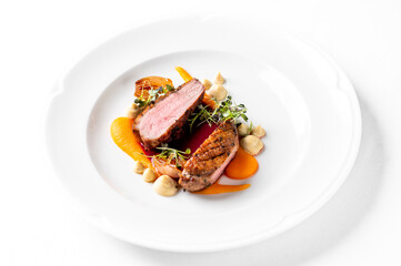 A pan-seared duck breast dish with crispy skin, sliced and elegantly plated with carrot pur&eacute;e, vegetables, and a red wine jus