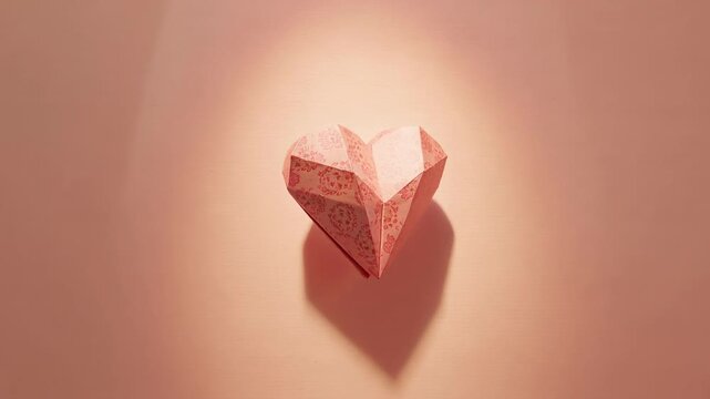 Shifting camera revealing origami heart on pink wall in studio, spotlight showing right facet