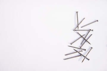 A pile of metal nails scattered on a white background casting shadows