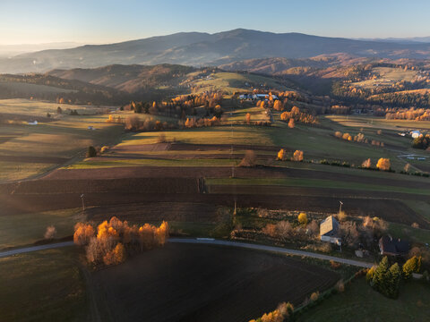 Aerial view of golden light paints the rolling fields and autumnal trees near the distant mountains, Detvianska Huta, Banska Bystrica Region, Slovakia.