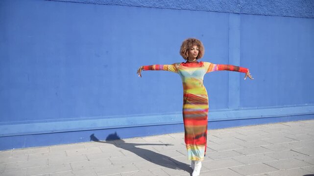 An Elegant Fashion Model Posing Gracefully Against a Bright Blue Wall Sporting a Colorful Dress