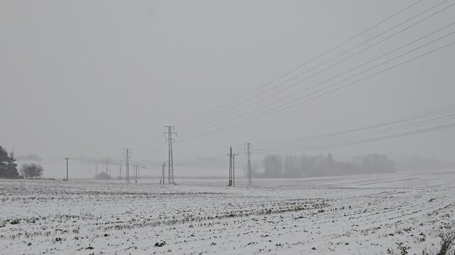 High voltage power line masts in fields during winter blizzard illustrating energy crisis and electricity infrastructure concept in Eastern Europe
