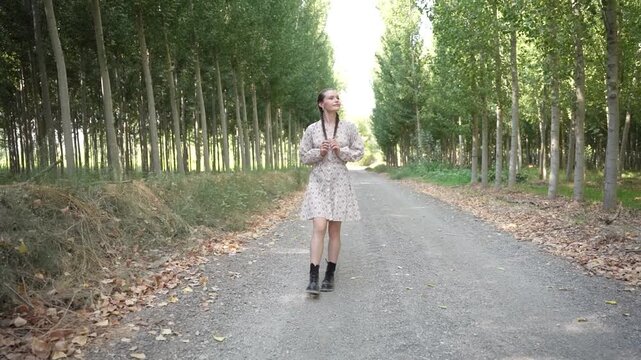 A Young Woman Delightfully Walking Along a Gravel Path That is Surrounded by Lush Trees