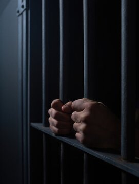 Hands grasping metal bars in a dimly lit prison cell, conveying a sense of confinement and despair. Prison life and isolation concept.