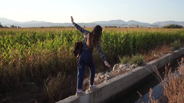 An Adventurous Young Woman is Walking Along a Scenic Canal Surrounded by Lush Green Fields