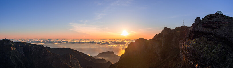 Fototapeta premium Ultra wide sunrise panorama from Pico do Arieiro Madeira Portugal high ridge, bright dawn lights sea of clouds above Atlantic cliffs valleys and distant island silhouettes seen from famous viewpoint
