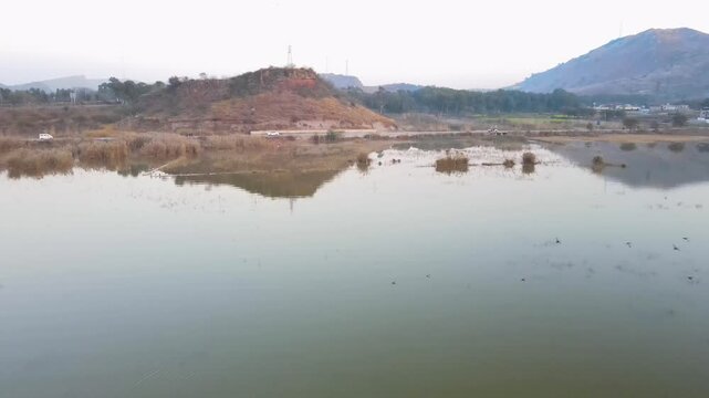 Aerial view of Kallar Kahar Lake reflecting hills in the calm water creating a serene, mirror-like effect, Kallar Kahar, Punjab, Pakistan.