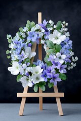 a floral wreath with blue and white flowers on an easel, against a black background