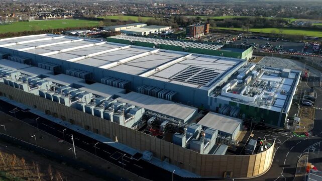 Aerial view of Google's new data centre, a colossal structure of whites and greys, framed by roads and greenery, Waltham Cross, United Kingdom.