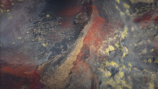 Aerial view of a Martian landscape with streaks of red iron oxides, black volcanic rock, and patches of green moss, Selfoss, Iceland.