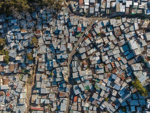 Aerial view of corrugated iron roofs baking under the harsh sun, with a winding road slicing through the dense settlement, Cape Town, Western Cape, South Africa.