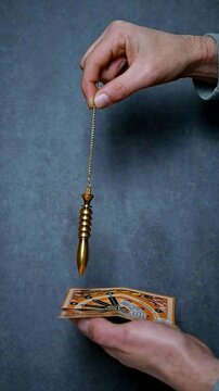 Radiesthesia Practice Using Golden Egyptian Pendulum Over Dowsing Chart on Blue Grey Background, Intuition and Energy Reading Concept, consulting the pendulum