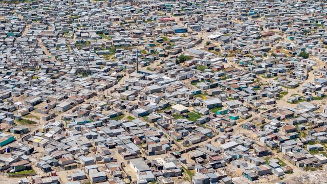 Aerial view of a dense, sprawling township blankets the landscape with a patchwork of corrugated iron roofs, pathways snaking through the settlement, Cape Town, Western Cape, South Africa.
