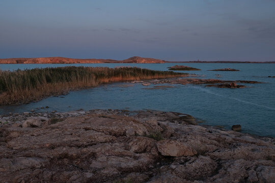 The tranquil landscape of Lake Balkhash in Kazakhstan at sunset or sunrise. The rocky shore and dense thickets of reeds emphasize the wild, untouched nature of this unique reservoir.
