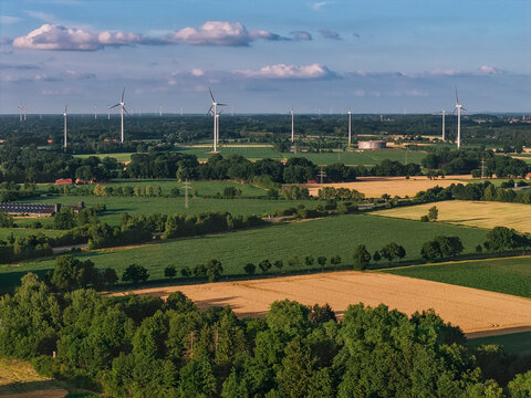 Aerial view of wind turbines standing tall against a backdrop of lush green fields and golden farmlands, creating a striking contrast of colors, Mullenbach, Rhineland-Palatinate, Germany.