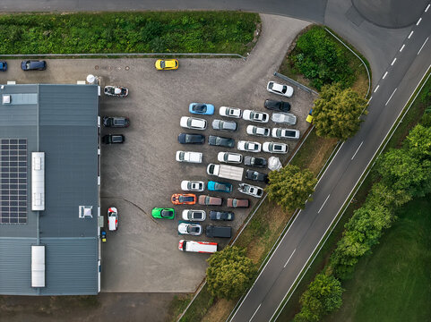 Aerial view of a parking lot filled with cars next to a building and a road, the scene bathed in the soft light of a late summer afternoon, Mullenbach, Rhineland-Palatinate, Germany.