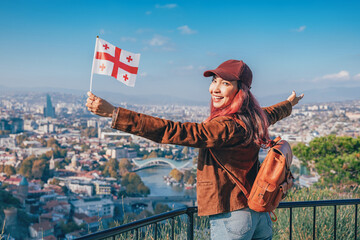 Cheerful woman holding a Georgia flag enjoying the panoramic view of Tbilisi cityscape and the Kura River © EdNurg