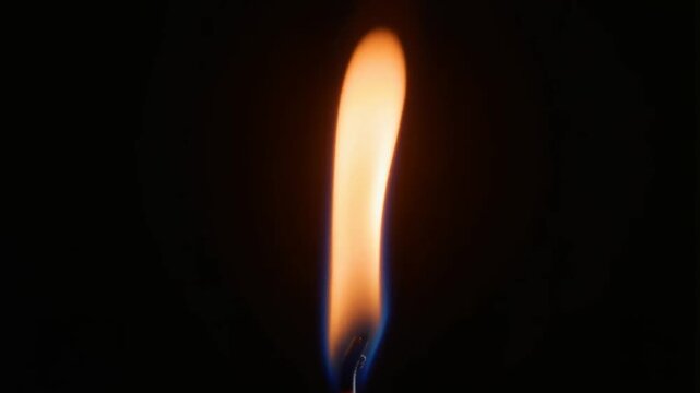 Close-up of a slow, steady candle flame with orange and amber glow isolated on black background, showing gentle flickering and natural fluid movement. Candle fire closeup warm light video footage