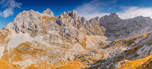 Obraz premium Rugged mountains defining a vast panoramic landscape, showing rocky peaks, steep slopes, and an expansive blue sky with clouds