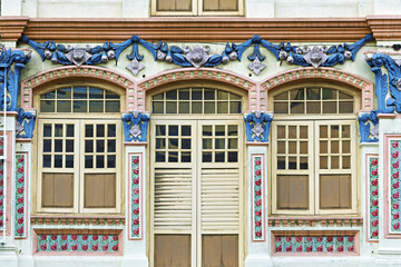 Fototapeta premium decorated facade along Jalan Besar Road, Singapore, known for its eclectic architectural heritage. The design features three large blue-framed windows with white panes, each crowned by sculpted arches