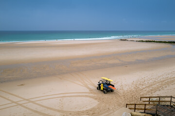 Lifeguard vehicle on sandy beach with surfers in the Atlantic Ocean, Lacanau, France
