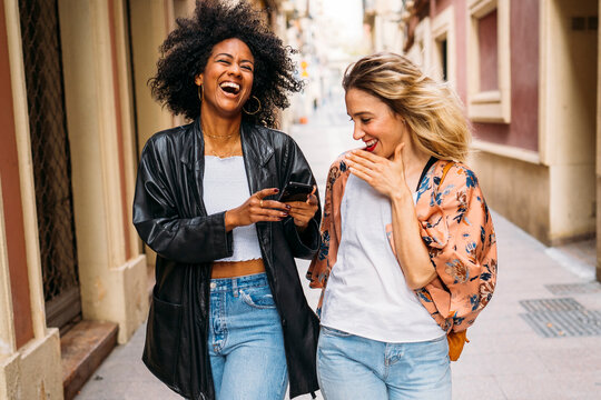 Friends walking and sharing smartphone content while laughing