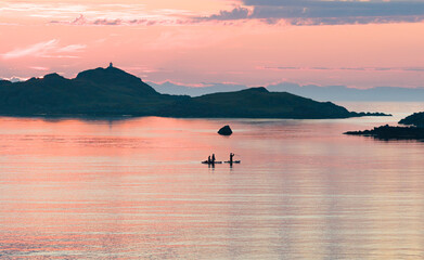 Midnight sun, evening, night. Amazing pink, orange sky, with reflection in the water of the sea, ocean. Some small rocky islands. 3 kayakers in the sea enjoying the light. Adventure, sports during mid © Dirk