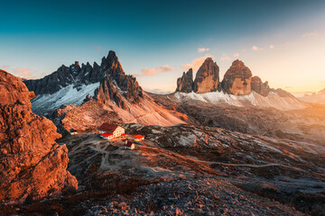 Fototapeta premium Alpine landscape of sunset over Tre Cime mountain peak and mountain hut during autumn in Dolomites, Italy