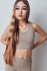 Young woman in beige sportswear standing against white background with long hair and confident...