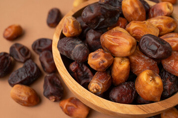 Obraz premium Dried dates in wooden bowl on brown background. Delicious sweet dried fruits flat lay top view. Date palm fruits, organic dates. Healthy vegan dessert