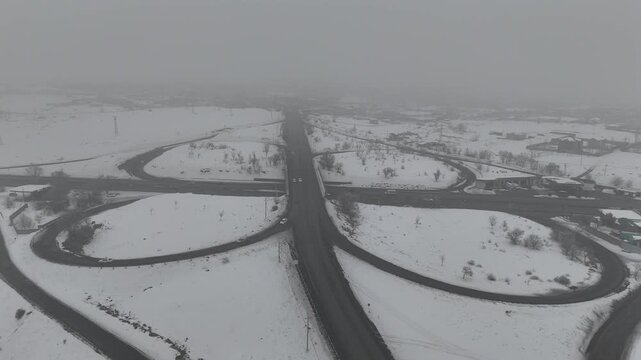 4K 60fps aerial view of a highway cloverleaf interchange in winter fog, cinematic snow-covered road infrastructure.