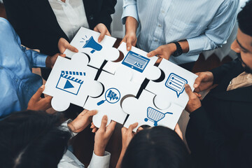 A diverse marketing team collaborates, holding puzzle pieces with symbols of technology, media, and...