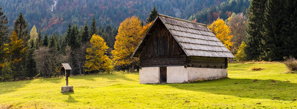 Rustic wooden barn with a stone base in a grassy field, surrounded by autumn trees. Bartolo Valley,Tarvisio,Friuli Venezia Giulia,Italy