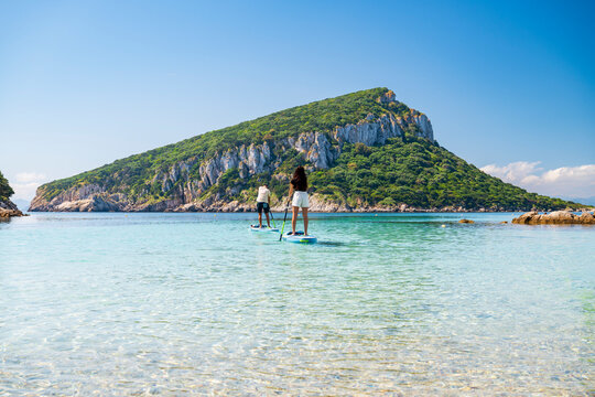 Couple paddleboarding on crystal clear turquoise sea near Figarolo Island, Golfo Aranci, Sardinia, Italy, on a sunny summer day