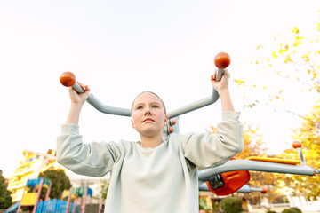 Teenage girl exercising on outdoor fitness equipment in park, strength training, active lifestyle, healthy childhood, sport and wellness concept
