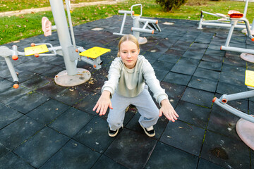 Teenage girl doing squat exercise on outdoor fitness playground, balance and coordination training, body control, healthy lifestyle, wellbeing and active childhood concept
