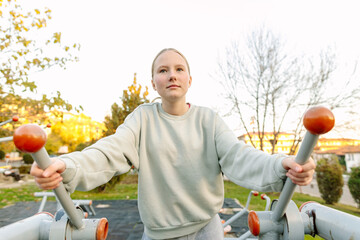 Teenage girl training on outdoor fitness equipment in city park, balance and coordination exercise, healthy lifestyle, body control and wellbeing concept

