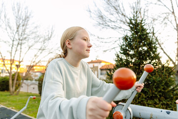 Teenage girl exercising on outdoor fitness equipment in city park, focused training, healthy lifestyle, concentration, balance and body control concept
