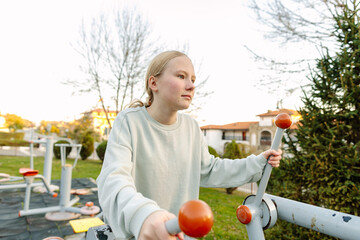 Teenage girl exercising on outdoor fitness equipment in city park, focused training, healthy lifestyle, concentration, balance and body control concept
